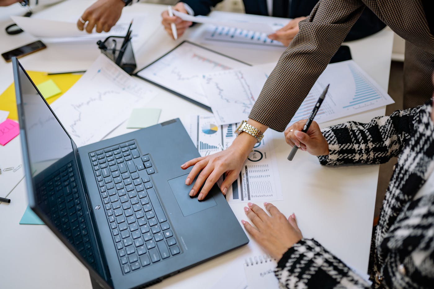 A person using a laptop while business charts and documents are reviewed in a meeting.