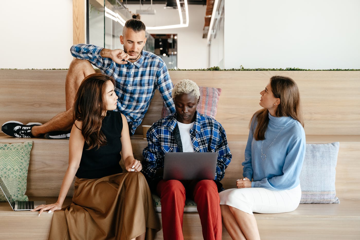 Four business professionals discussing work around a laptop in a modern office.
