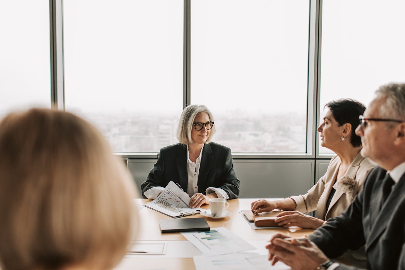 Executives in formal business attire discussing documents in a boardroom meeting.